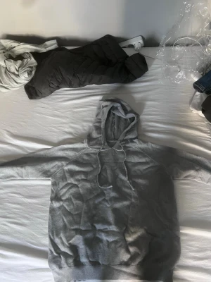 Grå hoodie med dragsko - En stilren grå hoodie gjord av merinoull med huva och dragsko. Hoodien har långa ärmar, ribbade muddar vid ärmslut och nederkant samt en klassisk passform. Perfekt för en avslappnad look och enkel att matcha med jeans eller joggers.