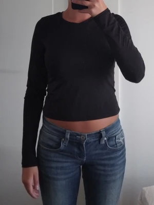 Svart långärmad croppad topp - En svart, långärmad och croppad topp med rund halsringning. Toppen har en slim passform och är tillverkad i ett mjukt och stretchigt material som känns lätt och luftigt. Ungefär som Tränings material