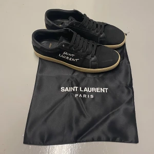 Svarta Saint Laurent sneakers - Snygga svarta sneakers från Saint Laurent med beige sula och handskriven logga på sidan. Skorna har snörning, rund tå och är tillverkade i en mix av skinn och mocka. Perfekta för dig som gillar stilrena och exklusiva detaljer. Vid intresse eller frågor är det bara att höra av sig. Pris går att diskutera 