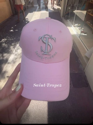 Ljusrosa keps Saint-Tropez - Snygg ljusrosa keps med broderad logga och texten Saint-Tropez framtill. Klassisk böjd skärm och justerbar baksida. Perfekt accessoar för en trendig look i sommar. Köpt i St Tropez!!