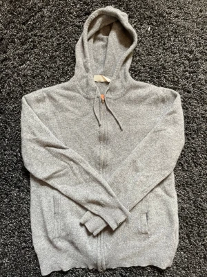 Grå zip hoodie med huva - Mysig grå hoodie med dragkedja framtill och justerbar huva. Tillverkad i mjukt material, perfekt för chill dagar. Har två fickor på sidorna och ribbade muddar vid ärmslut och nederkant. Enkel och stilren design som passar till det mesta.   Kom med frågor