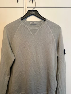 Stone Island - Ljusgrön sweatshirt från Stone Island med klassisk rund halsringning och ribbade muddar. Tröjan har den ikoniska svarta patchen med gult Stone Island-märke på ärmen. Perfekt för en avslappnad och stilren look. Storlek 14-16år junior men skulle säga att detta är en Small. Max andvända 5 ggr pris kan diskuteras.