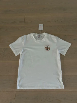 Vit Casablanca t-shirt med tryck - Säljer en vit t-shirt från Casablanca med färgglatt tryck och texten 'Casablanca Tennis Club' på ryggen. T-shirten har korta ärmar och rund hals. Perfekt för dig som gillar stilrena plagg med unika detaljer. Den sitter som en XS