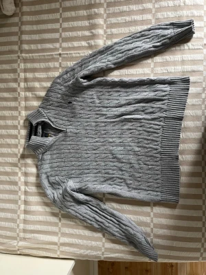 Grå kabelstickad tröja Polo Ralph Lauren - Snygg grå kabelstickad quarter zip från Polo Ralph Lauren. Tröjan har ribbade muddar och nederkant samt diskret logga på bröstet. Perfekt för dig som gillar klassisk och stilren design. Äkta. Passar dig som är 182-188. Mycket bra skick. Skriv för frågor eller fler bilder!