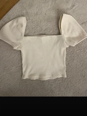 Vit ribbad topp med puffärmar H&M - Superfin vit ribbad topp från H&M med trendiga puffärmar och fyrkantig halsringning. Croppad modell som sitter snyggt och är perfekt till jeans eller kjol. Mjuk och stretchig i materialet för en bekväm känsla.