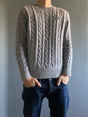 Ralph Lauren kabelstickad  - Snygg grå kabelstickad tröja med rund hals och ribbade muddar vid ärmslut och nederkant. Tröjan har ett diskret broderat märke på bröstet och är perfekt för lager på lager. Passar till både jeans och chinos. Det finns ingen lapp kvar men den är knappt använd och jag har kvar plast påsen som man får den i när man köper den ny. Man kan pruta ner priset vid snabb affär men inga skambud tack! 