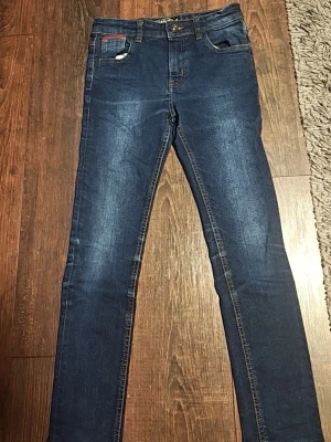 Mörkblå skinny jeans med brodyr - Snygga mörkblå skinny jeans med lätt slitning och klassisk femficksdesign. Jeansen har en liten gul brodyrdetalj på ena bakfickan och kontrastsömmar. Perfekta för dig som gillar en smal passform och tidlös look. Aldrig använda