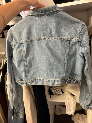 Ljusblå  jeansjacka - Trendig ljusblå  jeansjacka med slitna detaljer och två bröstfickor med lock. Klassisk krage och knappstängning framtill. 