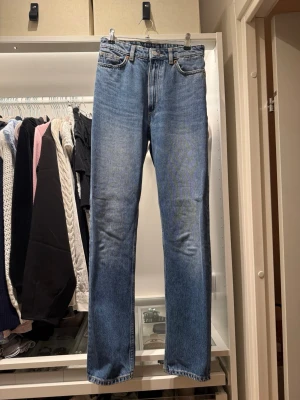 Blå raka jeans - Säljer ett par klassiska blå jeans med rak passform . Jeansen har fem fickor, bälteshällor och stängs med dragkedja och knapp. Materialet är denim i 100% bomull för en tidlös look. Midjemått 32,5cm , från midja till skrev 26cm , innrebenslängd 76 cm