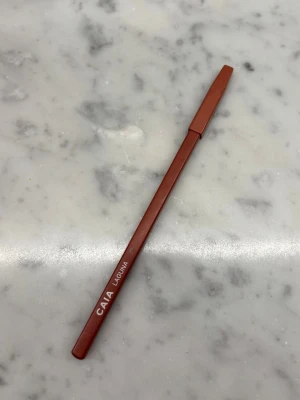 CAIA Läppenna Laguna - Snygg läppenna från CAIA i nyansen Laguna. Pennan har en varm brun/rosa ton och klassisk pennform med tillhörande lock. Perfekt för att definiera och forma läpparna med precision. Har vässats nån eller några enstaka gånger, längden nu är 16 cm 🩷