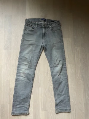 Grå slim fit jeans - Snygga grå slim fit jeans med klassisk femficksdesign och dragkedjegylf. Jeansen har en tvättad look och är tillverkade i ett stretchigt denimtyg för skön passform. Perfekta till en avslappnad stil.