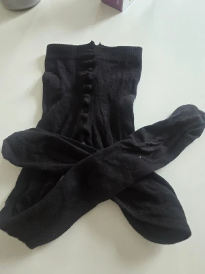 Svarta strumpbyxor från H&M - Säljer ett par svarta strumpbyxor från H&M i storlek 146/152. De har en enkel design med ribbad struktur längs benen och är tillverkade i mjuk bomullsmix som känns skön mot huden. Perfekta till både kjol och klänning.