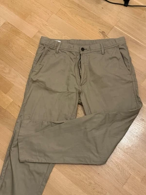 Beige chinos med raka ben - Snygga beige chinos med raka ben och klassisk passform. Byxorna har bälteshällor, sidofickor och en knappgylf. Tillverkade i ett mjukt och lätt material som passar perfekt till en avslappnad stil.