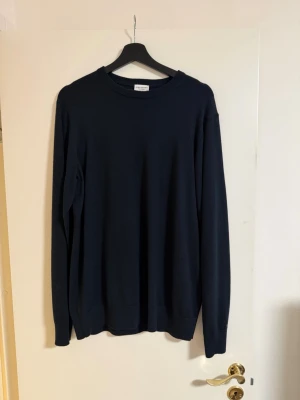 John Henric Tröja - En stilren mörkblå tröja med rund halsringning och långa ärmar. Tröjan har en enkel, klassisk design utan tryck eller mönster och är tillverkad i ett mjukt material som passar perfekt till alla outfits.
