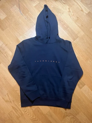 Mörkblå hoodie Jack & Jones - Säljer denna snygga mörkblå hoodie från Jack & Jones med orange logotyp på bröstet. Den är i storlek M men passar bättre för L Klassisk modell med huva och dragsko samt stor magficka framtill. Tillverkad i mjukt material som känns skönt mot huden. Perfekt för en avslappnad och trendig stil. Vid frågor, extra bilder eller liknande är det bara att kontakta mig!