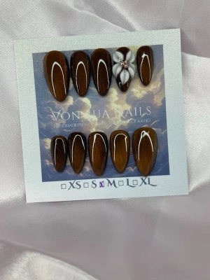 Chestnut (M);Medium Almond - Snygga handgjorda press-on naglar i en glansig cateye brun nyans med en medium lång mandelform. En nagel har en handgjord 3D-blomma i vitt med champange pärldetalj. Perfekt för dig som vill ha en trendig och elegant look.M: 16 mm, 12 mm, 12,5 mm, 11,5 mm, 10 mm
