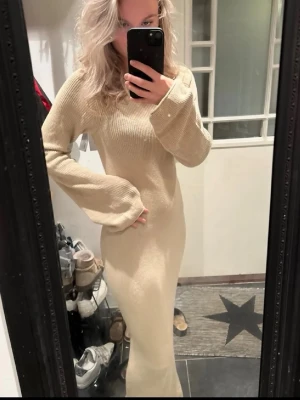 Beige stickad långklänning NAKD - Beige stickad långklänning med lång ärm och öppen rygg med snörningsdetalj. Mysig höstklänning från NAKD