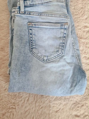 Ljusblå slitna raka jeans - Säljer ett par ljusblå jeans med raka ben och slitningar över knäna. Perfekta för en avslappnad och trendig look. Strl 146