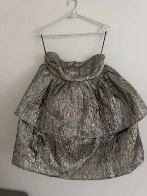 Glittrig silverklänning från AmyLynn - Glittrig kortklänning från AmyLynn i metallic silver med voluminösa lager och unik struktur. Klänningen är ärmlös och har en oversized siluett som ger en cool och trendig vibe. Perfekt för dig som vill sticka ut och älskar statementplagg.