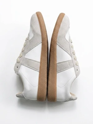 Mason Margiela skor - Stilrena sneakers i vitt läder med beige mockadetaljer och klassisk gummisula. Skorna har låga skaft och vita snören, perfekt för en clean och tidlös look. Passar till många olika outfits och har en retroinspirerad design.