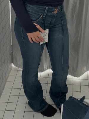 Mörkblå bootcut jeans med låg midja - Säljer ett par mörkblå bootcut jeans med hög midja och dubbla knappar i linningen. Jeansen har markerade sömmar framtill och klassisk femficksdesign. Materialet är denim med lätt stretch för skön passform. Perfekta till en trendig vardagslook. Från bershka i stockholm, finns ett litet litet hål mellan bena typ 1 cm. Använt knappt ett halvt år, väldigt fint skick annars🙃