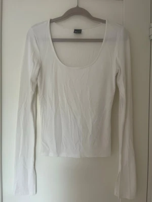 Vit långärmad topp från Gina Tricot - Säljer en vit långärmad topp från Gina Tricot med djup v-ringning. Toppen är tight i modellen och passar perfekt till både jeans och kjol. Tillverkad i mjukt material som känns skönt mot huden. Enkel och stilren design som är lätt att matcha.