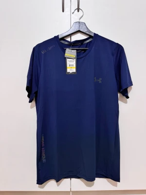 Mörkblå sport-tshirt Under Armour - Snygg mörkblå sport-tshirt från Under Armour med diskret logga på bröstet och tryck på axeln samt vid nederkanten. Tillverkad i ett lätt och snabbtorkande funktionsmaterial, perfekt för träning eller vardagsstil.