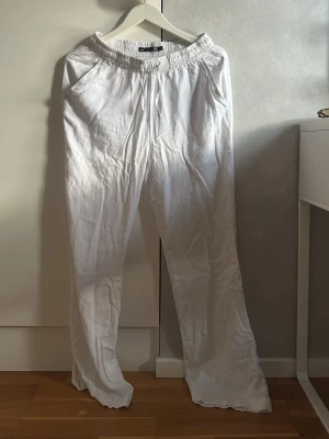 Vita linnebyxor med resårmidja - Säljer ett par vita linnebyxor med avslappnad passform och resår i midjan. Byxorna har snörning framtill, sidofickor och en bakficka. Perfekta för en chill och luftig stil under varma dagar. Dom är ganska vida hela vägen ner. Men annars perfekta. Aldrig använda. 