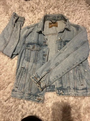 Ljusblå klassisk jeansjacka - Snygg ljusblå jeansjacka med raka linjer och klassiska detaljer som bröstfickor med knapp och silverfärgade knappar framtill. Storlek M men sitter mer som xs/s