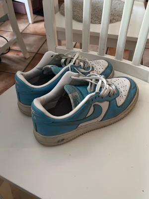 Blåvita airforces ( sneakers )  - Snygga sneakers i blått och vitt med klassisk låg siluett och vita skosnören. Ovandelen är i läder med perforerade detaljer på tån för extra ventilation. Yttersulan är vit med beige inslag. Perfekta för en avslappnad streetwear-look. 