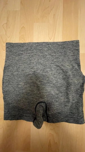 Gråmelerade träningshorts - Säljer ett par gråmelerade träningshorts i stretchigt material. De har hög midja och är väldigt sköna att ha på. Materialet är mjukt och sömlöst för extra komfort. Perfekta för dig som vill ha något bekvämt och funktionellt.