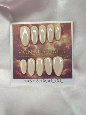 Avana (L);Medium Almond - Handgjorda press-on nails i en mjuk beige nude-nyans med glansig finish. En klassisk och stilren design med en varm neutral ton som passar till allt.  Form: Medium Long Almond Storlek: L 10 naglar ingår