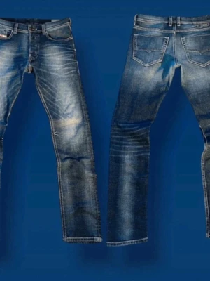 Blå slitna jeans från Diesel - Säljer ett par blå jeans från Diesel med snyggt slitna detaljer och tvättade effekter. Klassisk femficksmodell med raka ben och låg midja. Jeansen har Diesel Industry-märke på myntfickan och kontrastsömmar för en cool look. Jeansen har ett hål där bak