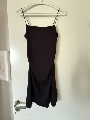 Svart kortklänning  - En stilren svart kortklänning med tunna axelband och enkel, rak siluett. Klänningen har en minimalistisk design och är perfekt för dig som gillar en klassisk look. 