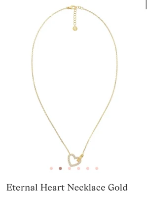 Guldhalsband med hjärthänge - Snyggt halsband i guld med ett hjärthänge dekorerat med gnistrande stenar. Hjärtat har en liten gulddetalj på sidan som ger en unik touch. Kedjan är tunn och elegant, perfekt för att lyfta vilken outfit som helst. Det är använt en del men inget som syns. 