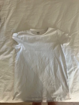 Vit basic t-shirt från 157 - En enkel vit t-shirt från 157 med rund hals och korta ärmar. Tillverkad i mjuk bomull, perfekt för en clean och avslappnad stil. Passar till allt och är ett måste i garderoben.