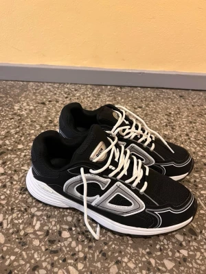 Skor  - Snygga svarta sneakers  med vita kontrastdetaljer och vita snören. Skorna har en chunky vit sula och stora CD-loggor på sidan. Ovandelen är i mesh och syntetmaterial för en sportig vibe. Perfekta för dig som vill sticka ut med stilrena och trendiga skor.