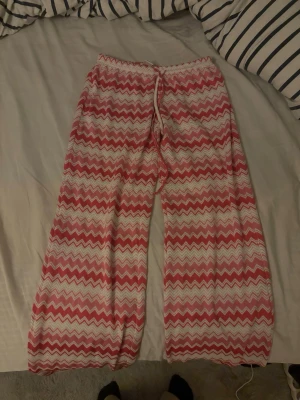 Mönstrade loungewear-byxor Gina Tricot - Säljer ett par mjuka och luftiga loungewear-byxor från Gina Tricot i storlek S. Byxorna har ett vågigt zigzag-mönster i rosa och vitt, med resårmidja. 