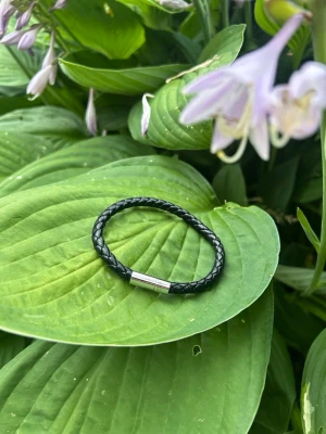 Svart flätat läderarmband - Stilrent svart armband i flätat läder med ett enkelt magnetlås i silverfärgad metall. Perfekt accessoar för en clean och modern look. Passar både tjejer och killar som gillar minimalistisk stil.
