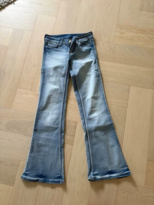 Jeans från Cheap Monday  - Säljer ett par blå bootcut jeans med snygg vintage tvätt och slitningar. Jeansen har fem fickor, gylf med dragkedja och knapp samt en orange patch bak i midjan. St 25/30