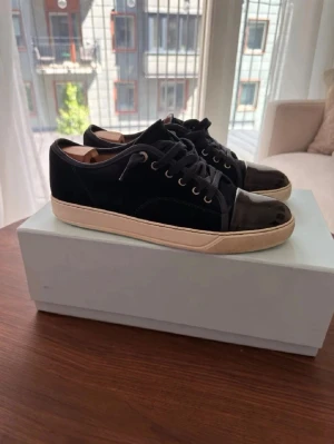 Svarta sneakers med lackdetaljer - Snygga svarta sneakers med coola lackdetaljer på tån och hälen. Skorna har svart mockaliknande material på sidorna, svarta skosnören och vit sula. Perfekta för dig som gillar en stilren men ändå unik look.