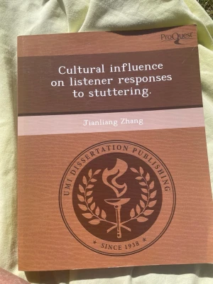 Cultural influence on listener responses - Bok med titeln 'Cultural influence on listener responses to stuttering' av Jianliang Zhang. Omslaget är brunt med vit text och har en logotyp för UMI Dissertation Publishing. Perfekt för dig som är intresserad av kultur och kommunikation.