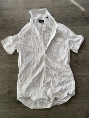 Vit kortärmad skjorta med knappar - Säljer en klassisk vit skjorta med korta ärmar och knappar framtill. Skjortan har en bröstficka och en snygg krage. Perfekt till sommarens outfits och enkel att matcha med det mesta.