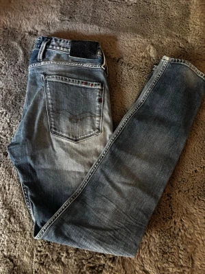 Blå tvättade raka jeans - Säljer ett par blå jeans med tvättad look och raka ben. Jeansen har klassiska bakfickor och bälteshällor. Materialet är denim och färgen är en snygg mellanblå med slitningar. Perfekta för en avslappnad stil.