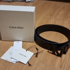 Svart skärp från Calvin Klein - INSTABOX!!! Snyggt svart skärp från Calvin Klein med stilren metallspänne i form av CK-loggan. Skärpet är gjort i slätt skinn och passar perfekt till jeans eller kostymbyxor. Levereras med originalbox och taggar kvar.