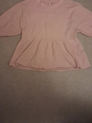 Ljusrosa peplum stickad tröja XXS - Supersöt ljusrosa stickad tröja med peplumskärning och rund hals. Tröjan har ribbstickad kant vid halsen och är tillverkad i ett mjukt material. Perfekt för dig som gillar en feminin och avslappnad stil.