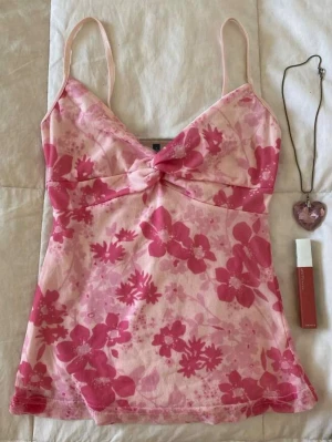 Blommig rosa linnetopp med twist - Söt linnetopp i ljusrosa med blommigt mönster i olika rosa nyanser. Toppen har smala axelband, twistad detalj framtill och ärmlös design. Perfekt för varma dagar och ger en Y2K - 2000s vibe till din outfit🩷