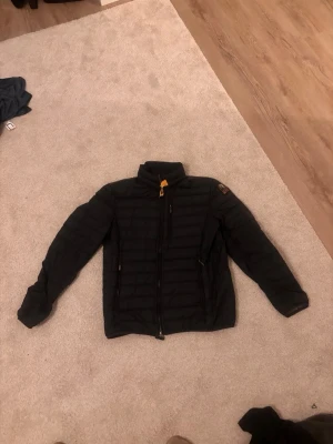 Svart dunjacka med hög krage - Snygg svart dunjacka med quiltat mönster och hög krage. Jackan har dragkedja framtill, två sidofickor med dragkedja och en patch på ena ärmen. Perfekt för kalla vinterdagar och riktigt skön att bära.lite skavanker här o där men går att patcha 