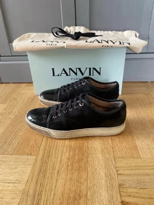 Svart Lanvin Cap-Toe – Box & Dustbag (Stl 43) - Svarta Lanvin cap-toe sneakers, UK 9 (EU 43), nyaste modellen. Mycket bra skick. Komplett set: box, dustbag och nya snören ingår (höger sko har nytt snöre påsatt). OBS: liten slitning på sulans undersida (ser ut som ett litet hål) – påverkar inget men nämns för transparens.