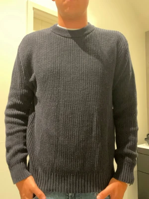 Mörkblå stickad tröja - En enkel och stilren mörkblå stickad tröja med rund halsringning och ribbade muddar vid ärmslut och nederkant. Tröjan har en rak passform och är perfekt till vinter eller höst.